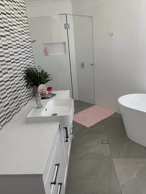 Bathroom with a black, white and grey mosaic feature wall, freestanding oval bath, white vanity and grey floor tile