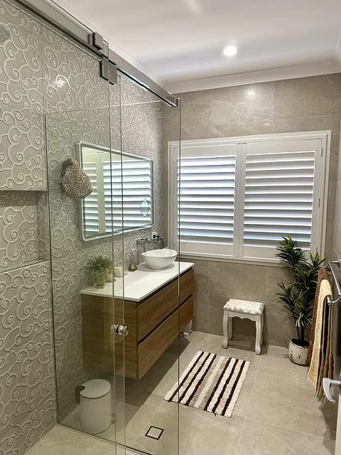 Shower with a textured patterned feature tile, stone-look wall tile, timber wall-hung vanity with a vessel basin and plantation shutters